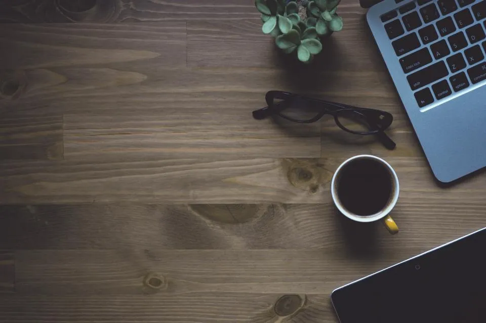 Laptop, glasses and a cup of coffee on a wooden work desk